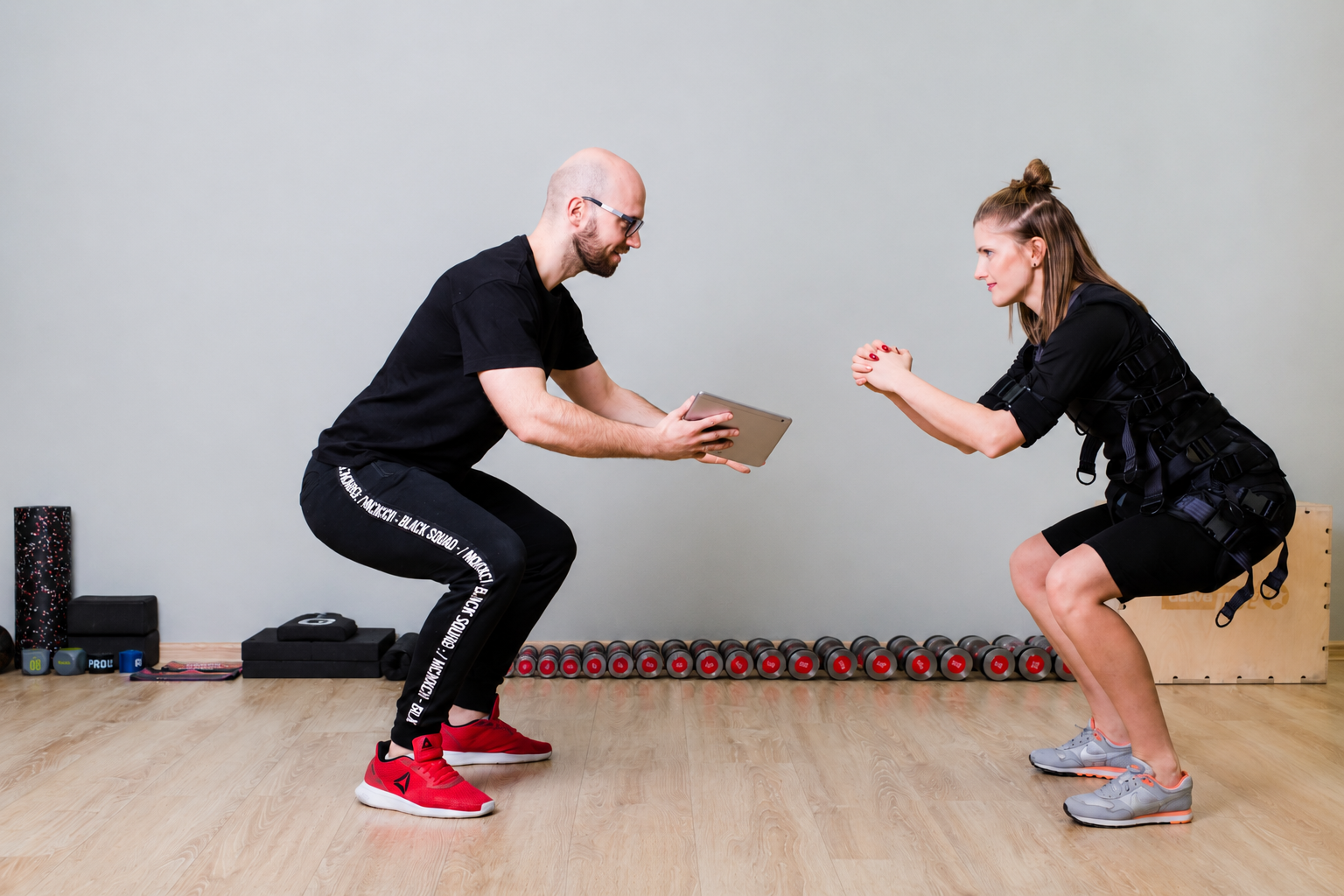 Trening EMS — przysiad z tabletem, trener obok klientki